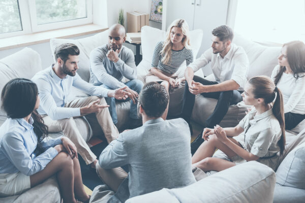 Group therapy. Group of young people sitting in circle while one man telling something and gesturing