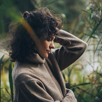 A tired woman sits in tall grass after exhausting herself because of her symptoms