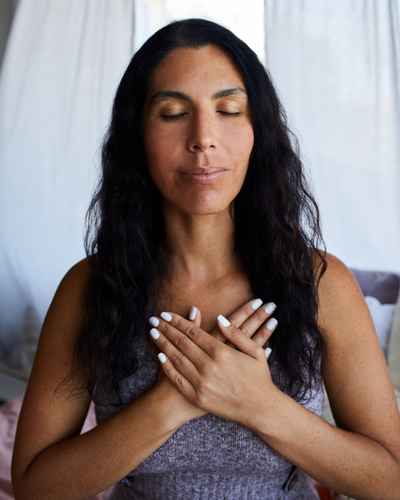 A woman holding her hands over her heart while internally using compassionate self-talk A woman holding her hands over her heart while internally using compassionate self-talk