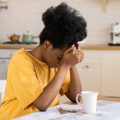 A Black woman is overwhelmed and discouraged, sitting at a table with paperwork A Black woman is overwhelmed and discouraged, sitting at a table with paperwork