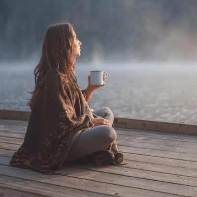 A woman relaxing in the early morning with a warm drink as part of her progress without consistency practice