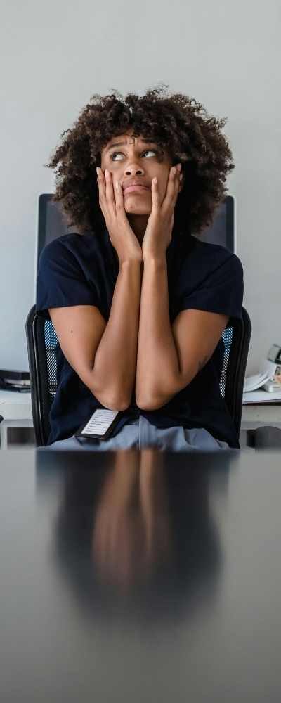 A Black woman sitting at a desk is overwhelmed, hands on her face A Black woman sitting at a desk is overwhelmed, hands on her face