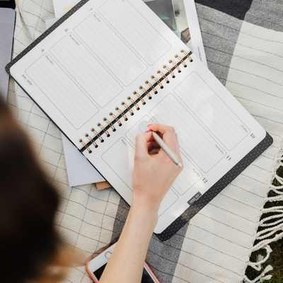 A white woman writes in a planner to stay organized A white woman writes in a planner to stay organized