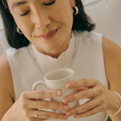 A woman with her eyes closed holding a mug smiles, using positive self-talk to support her executive function A woman with her eyes closed holding a mug smiles, using positive self-talk to support her executive function