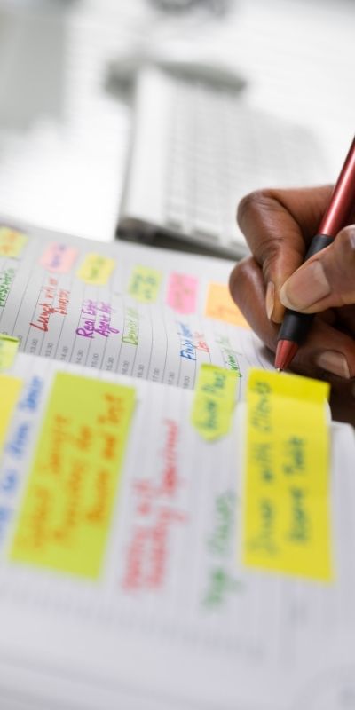 A woman writing in an agenda book that is color coded and has sticky notes A woman writing in an agenda book that is color coded and has sticky notes