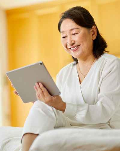 Happy woman smiling at her tablet because she's relaxed and reaching her goals by being proactive Happy woman smiling at her tablet because she's relaxed and reaching her goals by being proactive