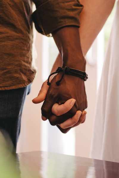 A closeup of two people holding hands in front of a window and curtains A closeup of two people holding hands in front of a window and curtains