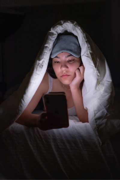 A woman scrolls her phone in bed because her ADHD causes trouble sleeping A woman scrolls her phone in bed because her ADHD causes trouble sleeping