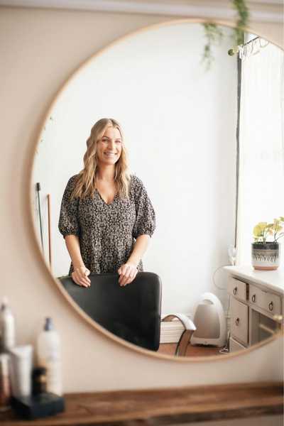 A blonde woman smiles in the reflection of a mirror on the wall while practicing her communication techniques for fast tangential talking