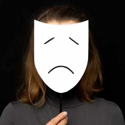 A woman holds a mask of a sad face in front of her face - emotions that are visible can often hide the true emotions beneath
