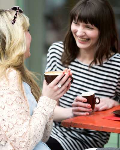Two friends talking and laughing together while holding mugs at a counter