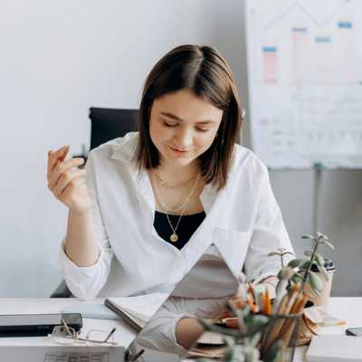 A calm, focused woman holding a pencil while looking at a notebook and smiling because she's no longer stressed by the avoidance-urgency cycle