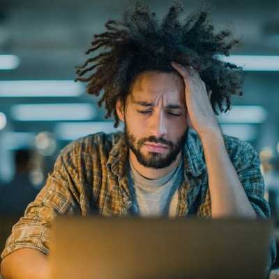 A man with his hand on his head while working late in front of a computer A man with his hand on his head while working late in front of a computer