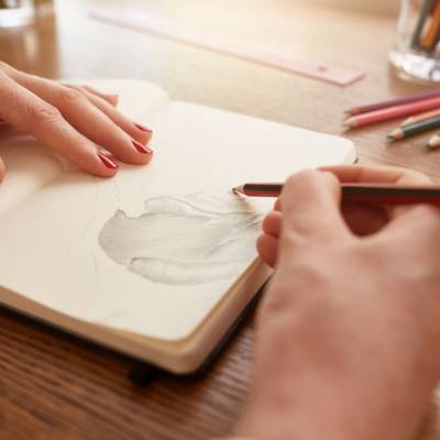 A woman's hands as she sketches in an open sketchbook for fun and to help her executive functioning skills