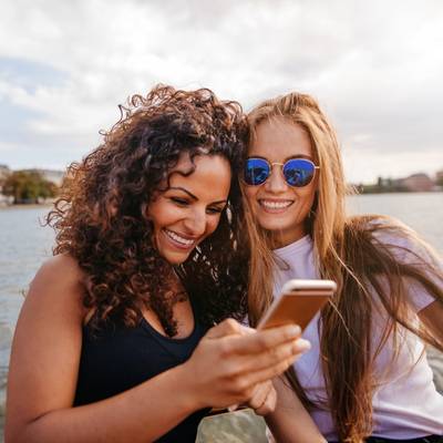 Two friends having a calm hang-out day by the water and looking together at one's phone