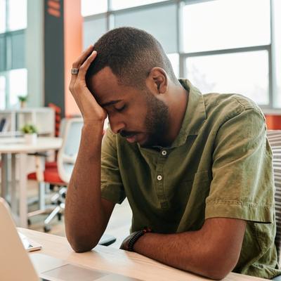 A man sits at a desk with his head in his hand experiencing burnout