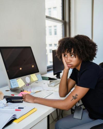 An overwhelmed woman sits at her desk surrounded by reminders