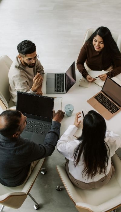 A group of coworkers seated at a table with laptops to show an example of all the small decisions that must get made at work for task and social reasons
