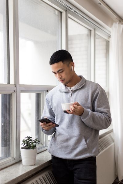 A person stands by the window scrolling on their phone because decision fatigue makes that easier than choosing a task to start