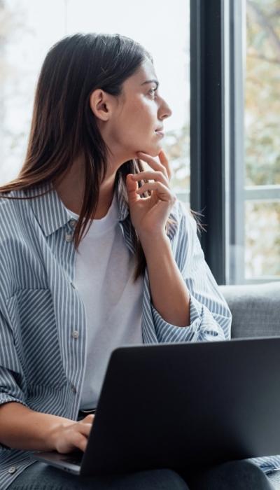 A woman looks out a window instead of at her laptop because she's distracted by internal interruptions