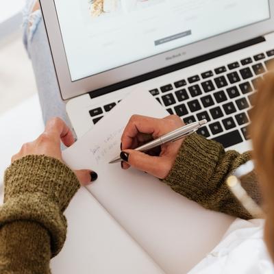 Leaving a note before switching tasks due to interruption can help make restarting easier as demonstrated by this woman making notes in her notebook on her laptop